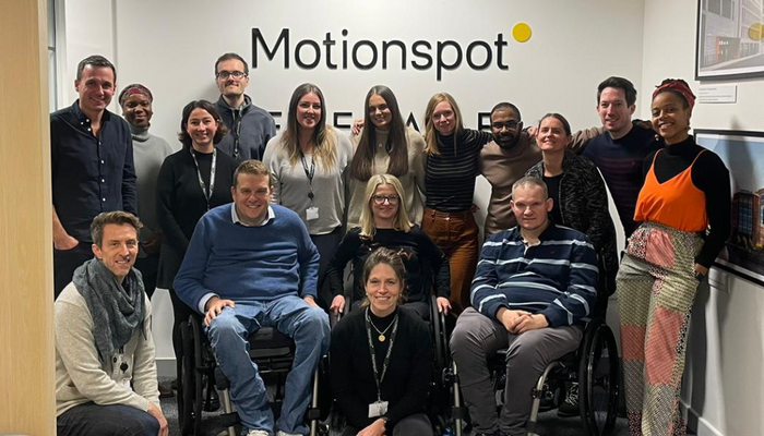 Group shot of Motionspot team smiling in front of the Motionspot logo in their design studio