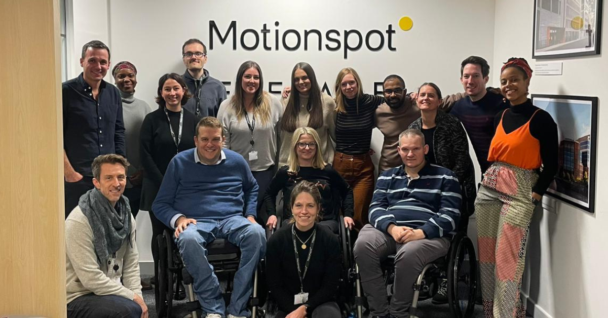 Group shot of Motionspot team smiling in front of the Motionspot logo in their design studio