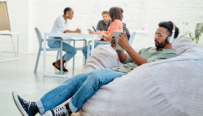 Group of people in an office setting, three at a table, one on a beanbag wearing headphones