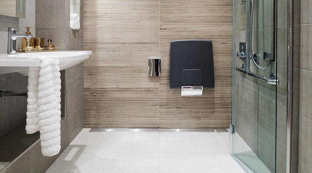 Residential bathroom focusing on accessible shower, horizontal light wood panelled wall with contrasting grey wall tiles and chrome detail finishes.