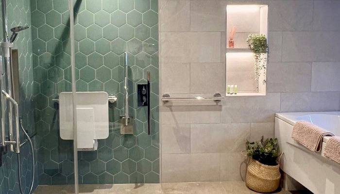 AbleStay's accessible bathroom including hexagon tiles in Timeless Jade, shower arm, hose and valve, bi-folding shower screen, chrome grab rails and wall mounted shower seat