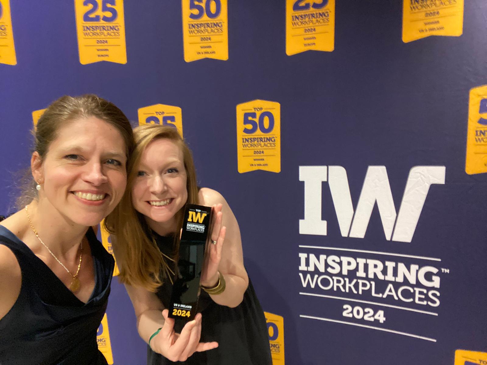 Julia and Laura from Motionspot holding the inspiring workplace award in front of a inspiring workplace backdrop